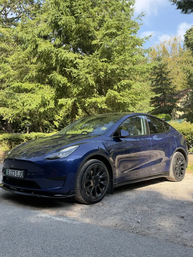Blue EV Rider Tesla Model Y parked beside trees